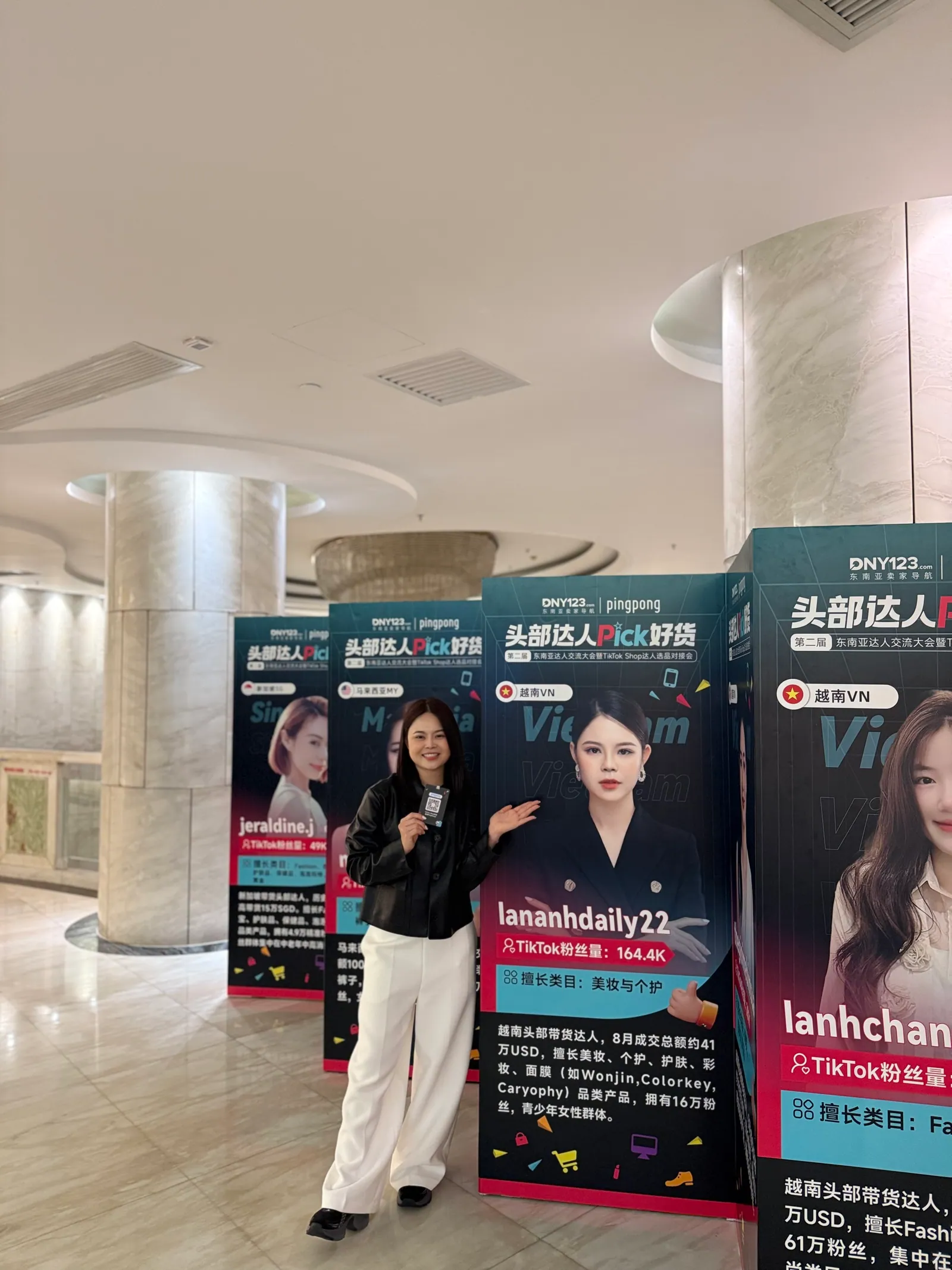 Một người đứng cạnh các standee in hình và tên kênh của nhà sáng tạo tại sảnh một sự kiện.